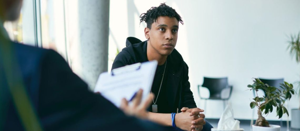 Black teenage boy having counselling with mental health professional during therapy session.